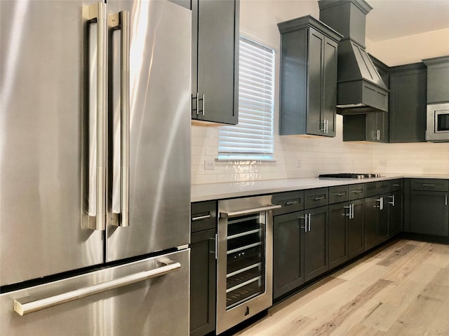 kitchen featuring premium range hood, beverage cooler, decorative backsplash, stainless steel appliances, and light hardwood / wood-style flooring