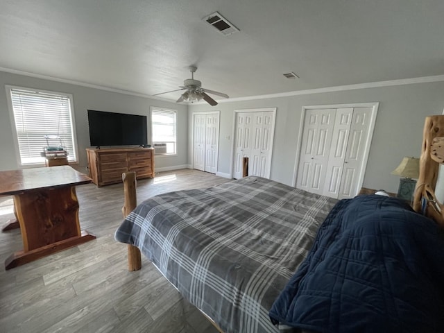 bedroom with crown molding, ceiling fan, multiple closets, and light hardwood / wood-style floors