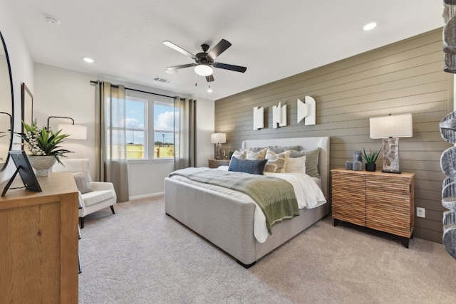 bedroom with light carpet, ceiling fan, and wood walls