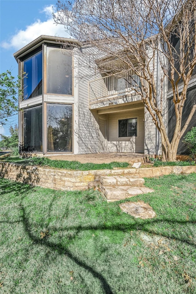 rear view of property featuring a balcony and a yard