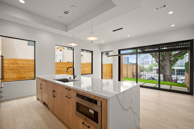 kitchen with sink, hanging light fixtures, light hardwood / wood-style floors, light stone counters, and a spacious island