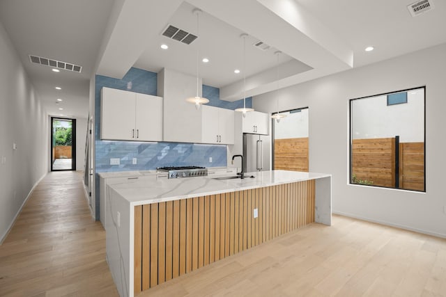 kitchen with high end fridge, hanging light fixtures, a large island, light stone countertops, and white cabinets