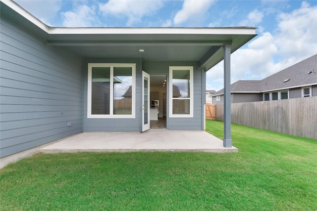 view of exterior entry featuring a lawn, a patio, and fence