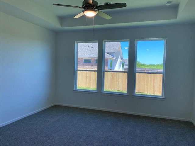 spare room featuring a tray ceiling, dark carpet, a healthy amount of sunlight, and ceiling fan