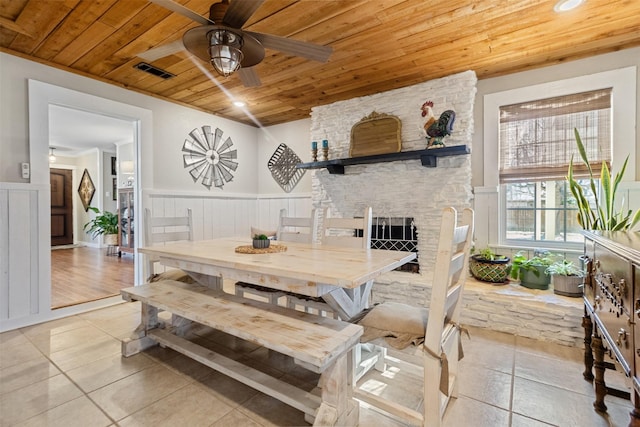 dining space featuring light tile patterned flooring, ceiling fan, wooden ceiling, and a fireplace