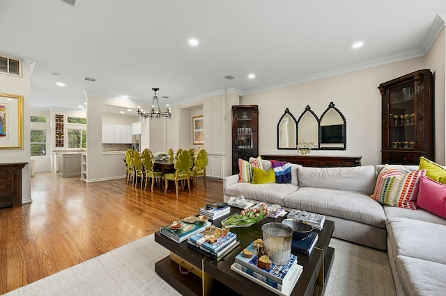 living room featuring an inviting chandelier, ornamental molding, and light wood-type flooring