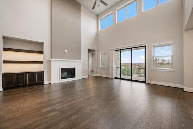 5801 Davenport Divide Rd, Austin, TX 78738 - unfurnished living room with ceiling fan, a towering ceiling, dark wood-style floors, and a glass covered fireplace