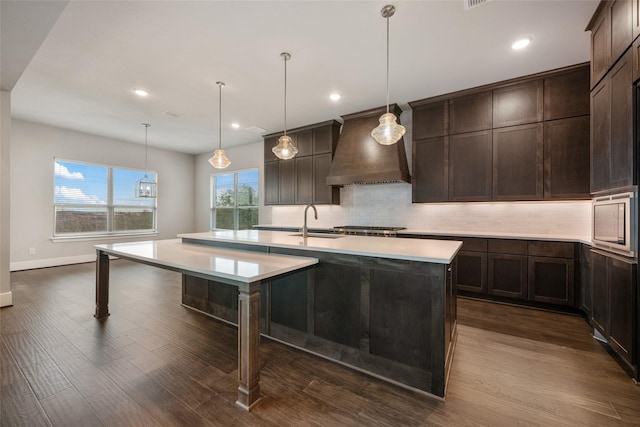 kitchen with pendant lighting, sink, custom range hood, and a center island with sink