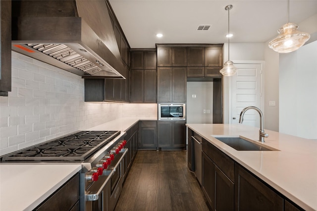 kitchen with sink, tasteful backsplash, hanging light fixtures, range with two ovens, and wall chimney range hood