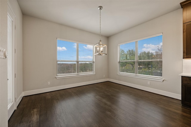 unfurnished dining area featuring a healthy amount of sunlight, an inviting chandelier, and dark hardwood / wood-style flooring