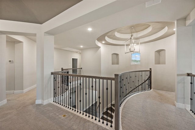 hallway featuring light carpet, a tray ceiling, and an inviting chandelier