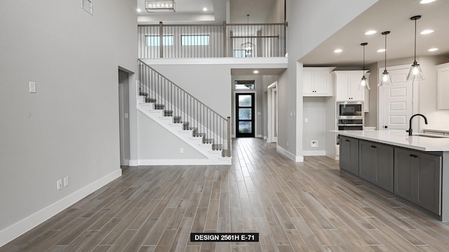 kitchen with gray cabinets, a towering ceiling, decorative light fixtures, white cabinetry, and sink