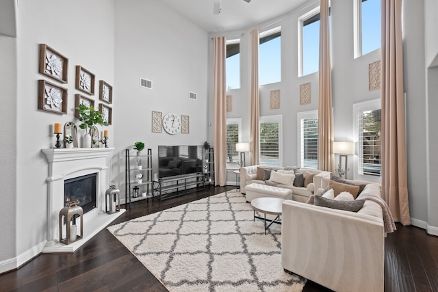 living room featuring a towering ceiling, a healthy amount of sunlight, and dark hardwood / wood-style floors