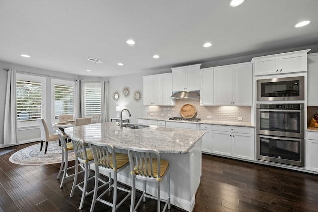 kitchen with sink, stainless steel appliances, light stone countertops, and a center island with sink