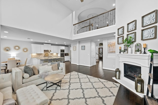 living room with ceiling fan, a towering ceiling, and dark hardwood / wood-style flooring