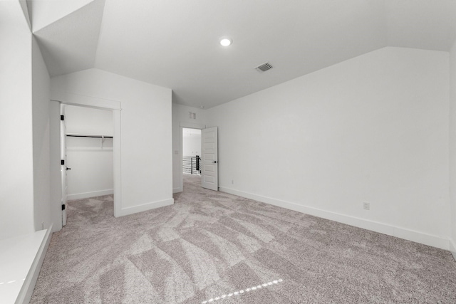 unfurnished bedroom featuring a walk in closet, lofted ceiling, light carpet, and a closet