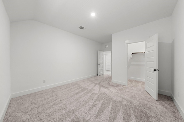 unfurnished bedroom featuring a walk in closet, lofted ceiling, light colored carpet, and a closet