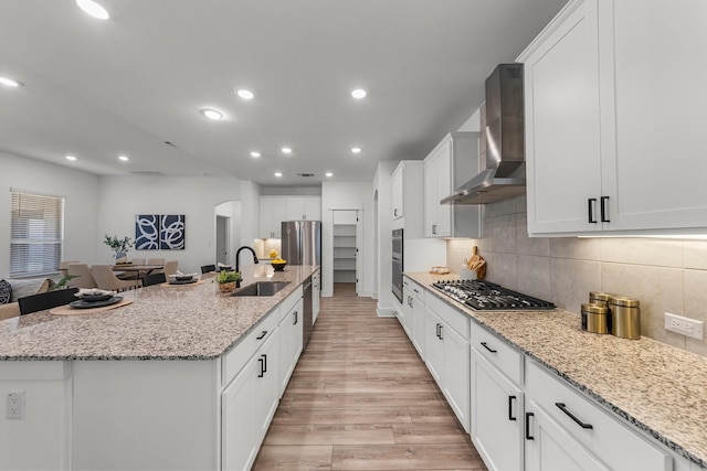 kitchen featuring appliances with stainless steel finishes, wall chimney exhaust hood, a large island, and light stone countertops