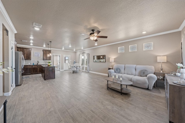 living room featuring sink, crown molding, a textured ceiling, and ceiling fan