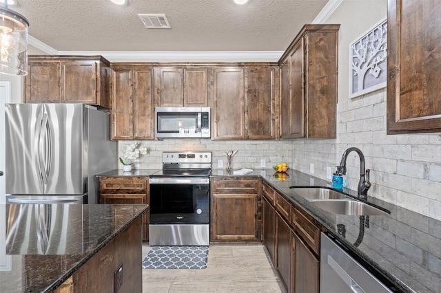 kitchen with sink, dark stone countertops, ornamental molding, stainless steel appliances, and a textured ceiling