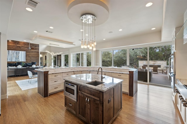 kitchen with sink, decorative light fixtures, a center island with sink, stainless steel microwave, and light stone countertops