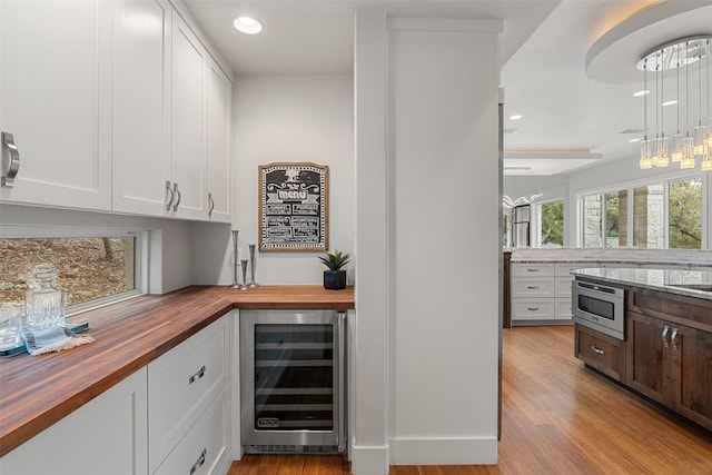 bar with white cabinets, stainless steel microwave, beverage cooler, and wood counters