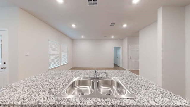 kitchen featuring sink, a kitchen island with sink, light stone counters, and light wood-type flooring