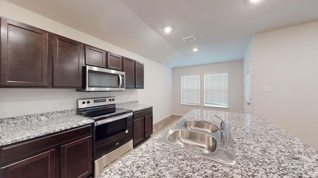 kitchen featuring vaulted ceiling, sink, light stone counters, stainless steel appliances, and dark brown cabinets