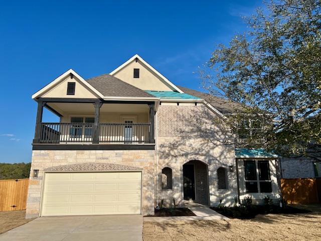 view of front of house with stucco siding, an attached garage, fence, a balcony, and driveway