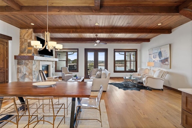 dining area featuring a stone fireplace, light hardwood / wood-style floors, beam ceiling, and wooden ceiling