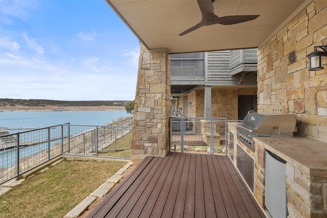 wooden deck featuring area for grilling, an outdoor kitchen, ceiling fan, and a water view