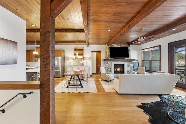 living room featuring light wood-type flooring, a large fireplace, ceiling fan, wood ceiling, and beam ceiling