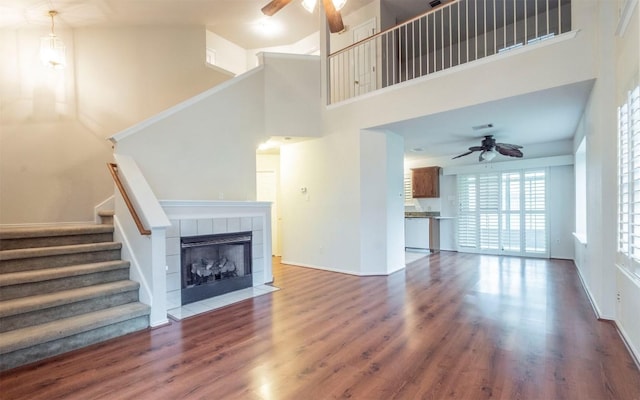 unfurnished living room featuring dark hardwood / wood-style flooring, a towering ceiling, ceiling fan, and a tiled fireplace