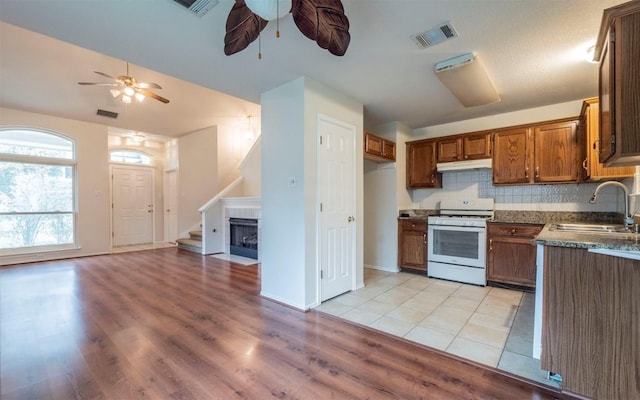 kitchen featuring sink, white range with gas stovetop, ceiling fan, tasteful backsplash, and a fireplace