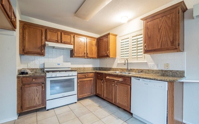 kitchen featuring dark stone countertops, sink, light tile patterned floors, and white appliances