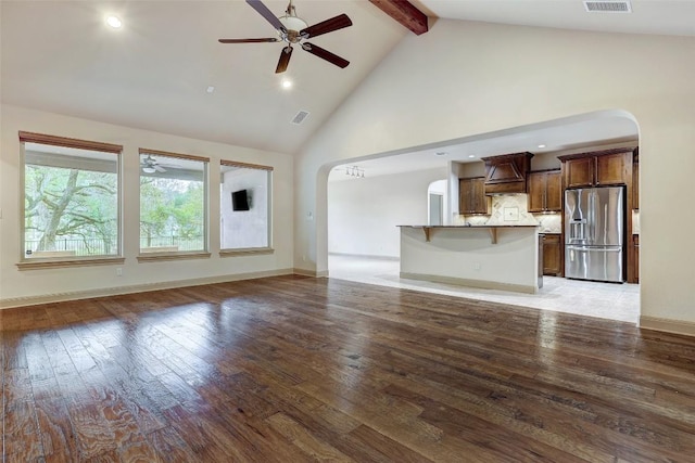 unfurnished living room with ceiling fan, beam ceiling, high vaulted ceiling, and light wood-type flooring