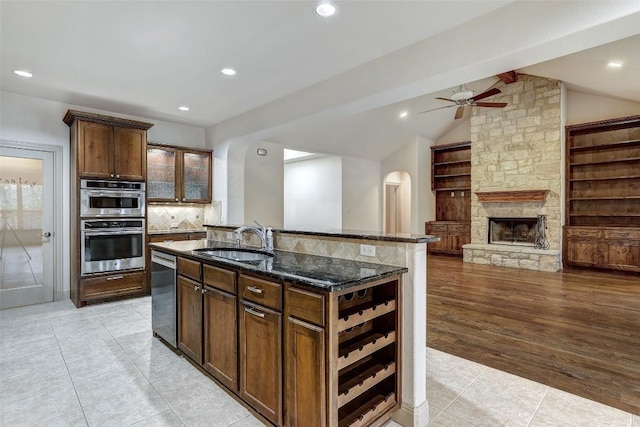 kitchen with sink, appliances with stainless steel finishes, an island with sink, vaulted ceiling, and dark stone counters