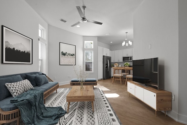 living area featuring baseboards, recessed lighting, light wood-style floors, visible vents, and ceiling fan with notable chandelier