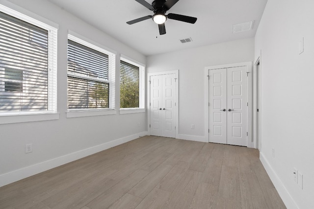 unfurnished bedroom featuring multiple closets, ceiling fan, and light wood-type flooring