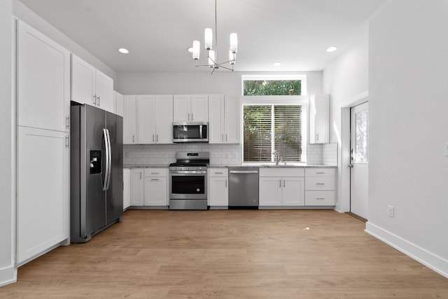 kitchen featuring stainless steel appliances, white cabinetry, light hardwood / wood-style floors, and decorative light fixtures