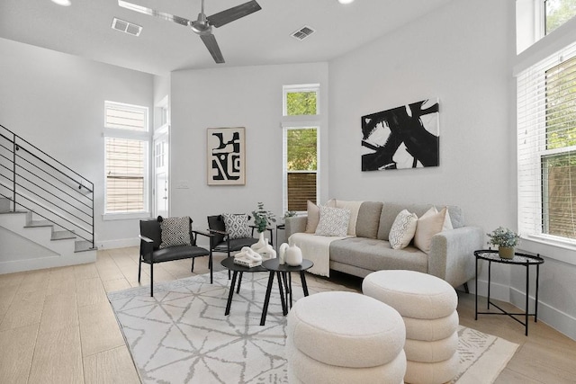 living area featuring wood finished floors, ceiling fan, visible vents, and stairs