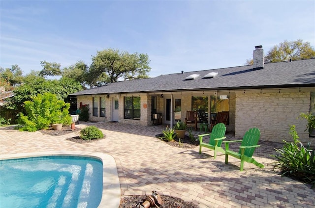back of property featuring a patio, a chimney, stone siding, and an outdoor pool