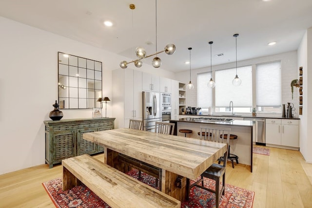 kitchen with sink, appliances with stainless steel finishes, light hardwood / wood-style floors, white cabinets, and decorative light fixtures