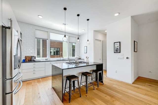 kitchen with appliances with stainless steel finishes, white cabinets, hanging light fixtures, a center island, and light hardwood / wood-style floors