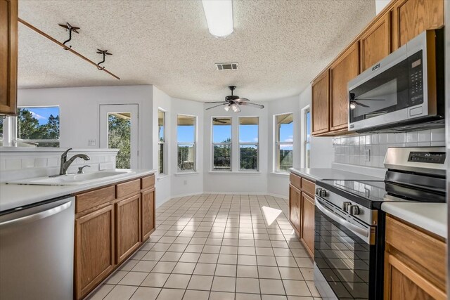 kitchen featuring sink, light tile patterned floors, appliances with stainless steel finishes, backsplash, and a textured ceiling