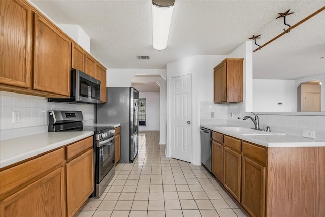 kitchen with sink, light tile patterned floors, appliances with stainless steel finishes, tasteful backsplash, and a textured ceiling