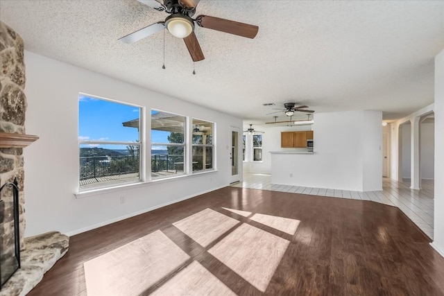 unfurnished living room featuring wood-type flooring, a stone fireplace, ceiling fan, and a textured ceiling