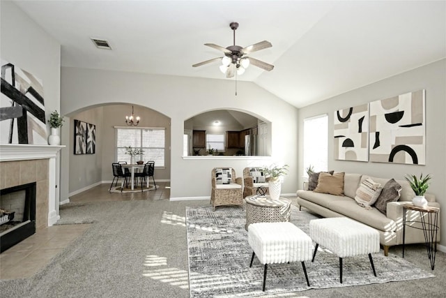 carpeted living room with ceiling fan with notable chandelier, plenty of natural light, a tiled fireplace, and vaulted ceiling