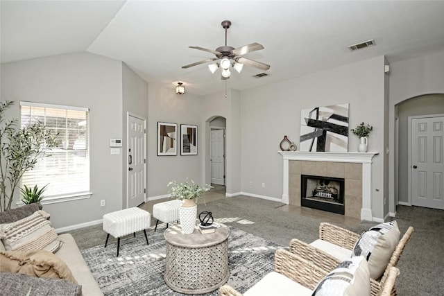 carpeted living room with ceiling fan, lofted ceiling, and a tiled fireplace