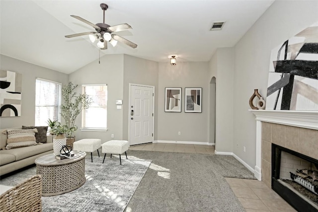 carpeted living room with a tile fireplace, vaulted ceiling, and ceiling fan